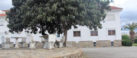 A building with a stone wall, outdoor seating, and a large tree in front.