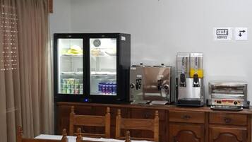 A dining area with a table set for two, a refrigerator, and a coffee machine.