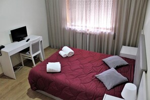 Quarto de hotel com cama, escrivaninha e computador, além de televisão.