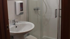 Casa de banho moderna com cabine de chuveiro de vidro, lavatório branco e espelho.