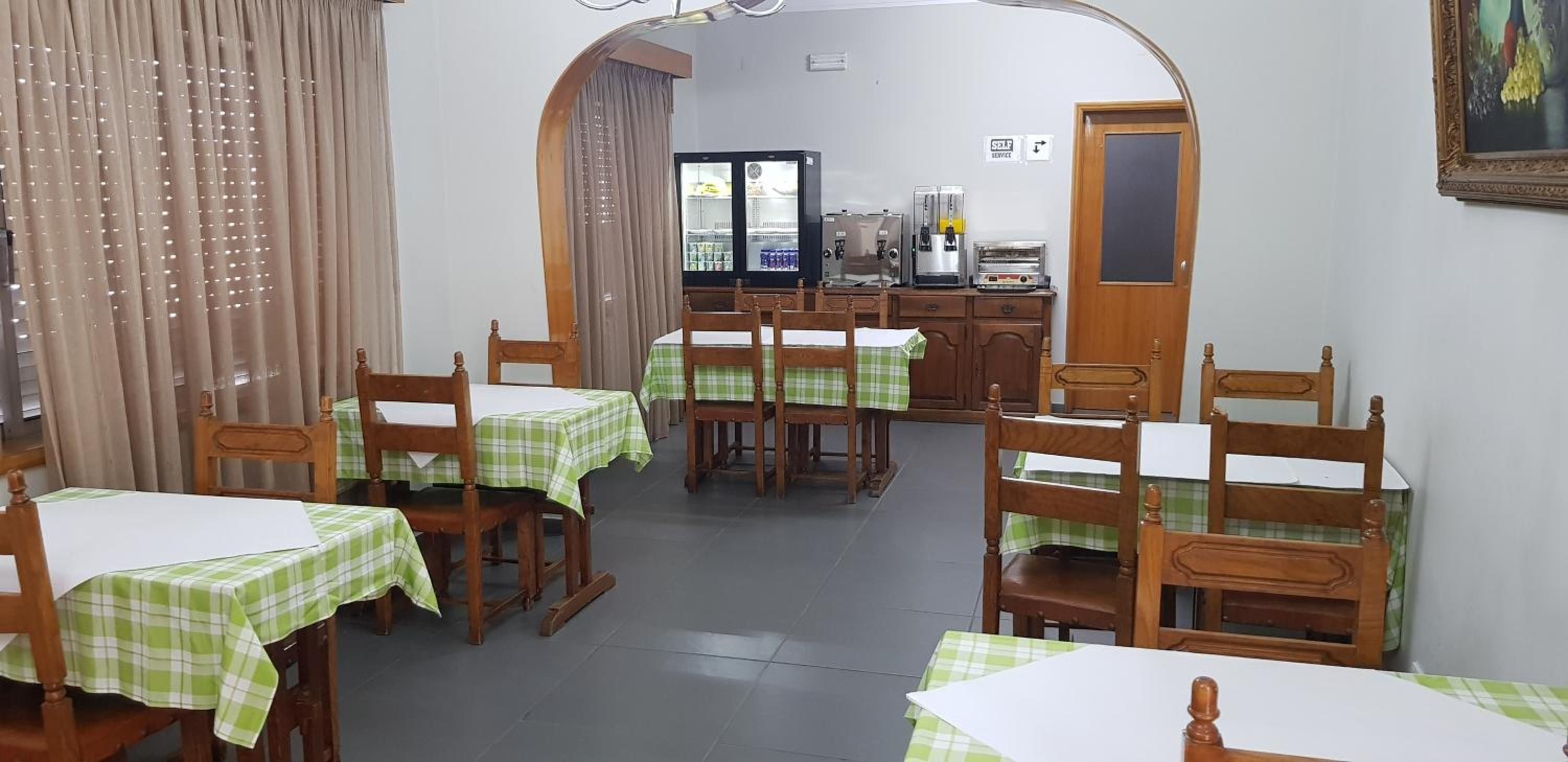 A dining area with tables and chairs, a refrigerator, and a self-service coffee machine.