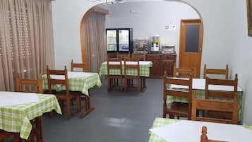 A dining area with tables and chairs, a refrigerator, and a self-service coffee machine.