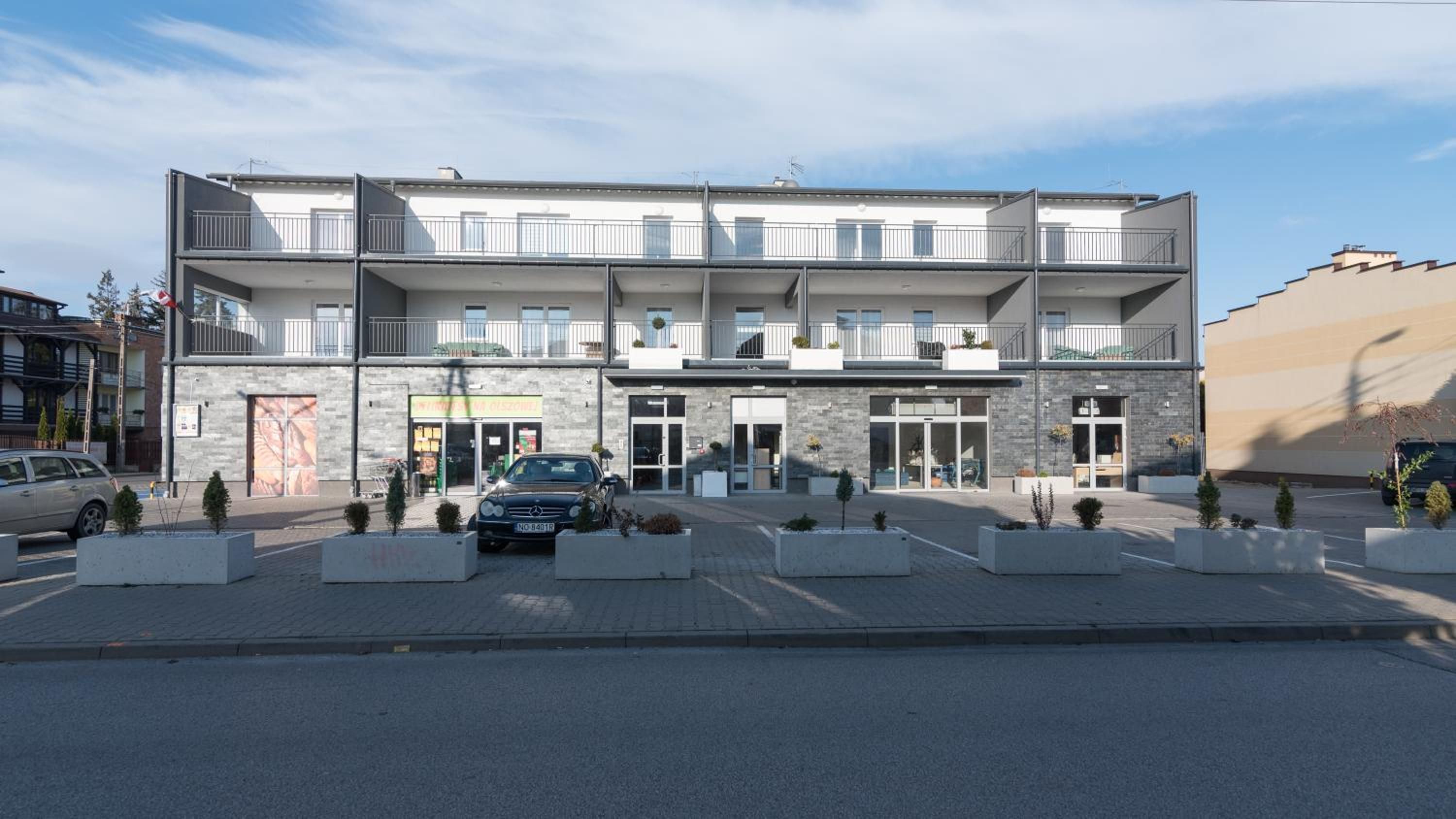 Ein mehrstöckiges Gebäude mit einem zentralen Eingang, Balkonen und einem Parkplatz.