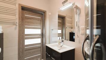 A modern bathroom with a wooden door, a white sink, a mirror, and a hairdryer.
