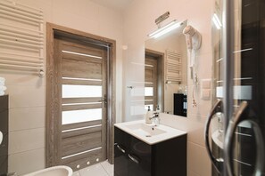 Een moderne badkamer met een houten deur, een wit wastafelmeubel, een spiegel en een haardroger.