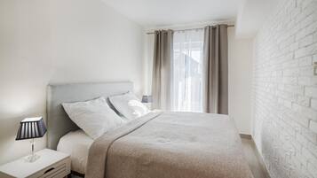 A bedroom with a bed, a nightstand, a lamp, and a window with curtains.