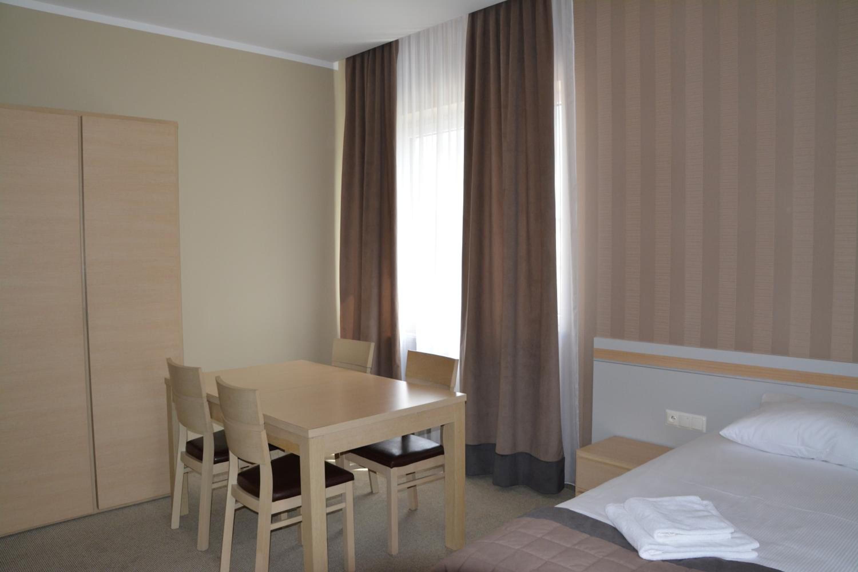 A hotel room with a bed, a desk, two chairs, a wardrobe, and a window with curtains.