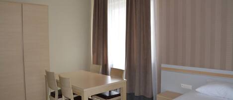 A hotel room with a bed, a desk, two chairs, a wardrobe, and a window with curtains.