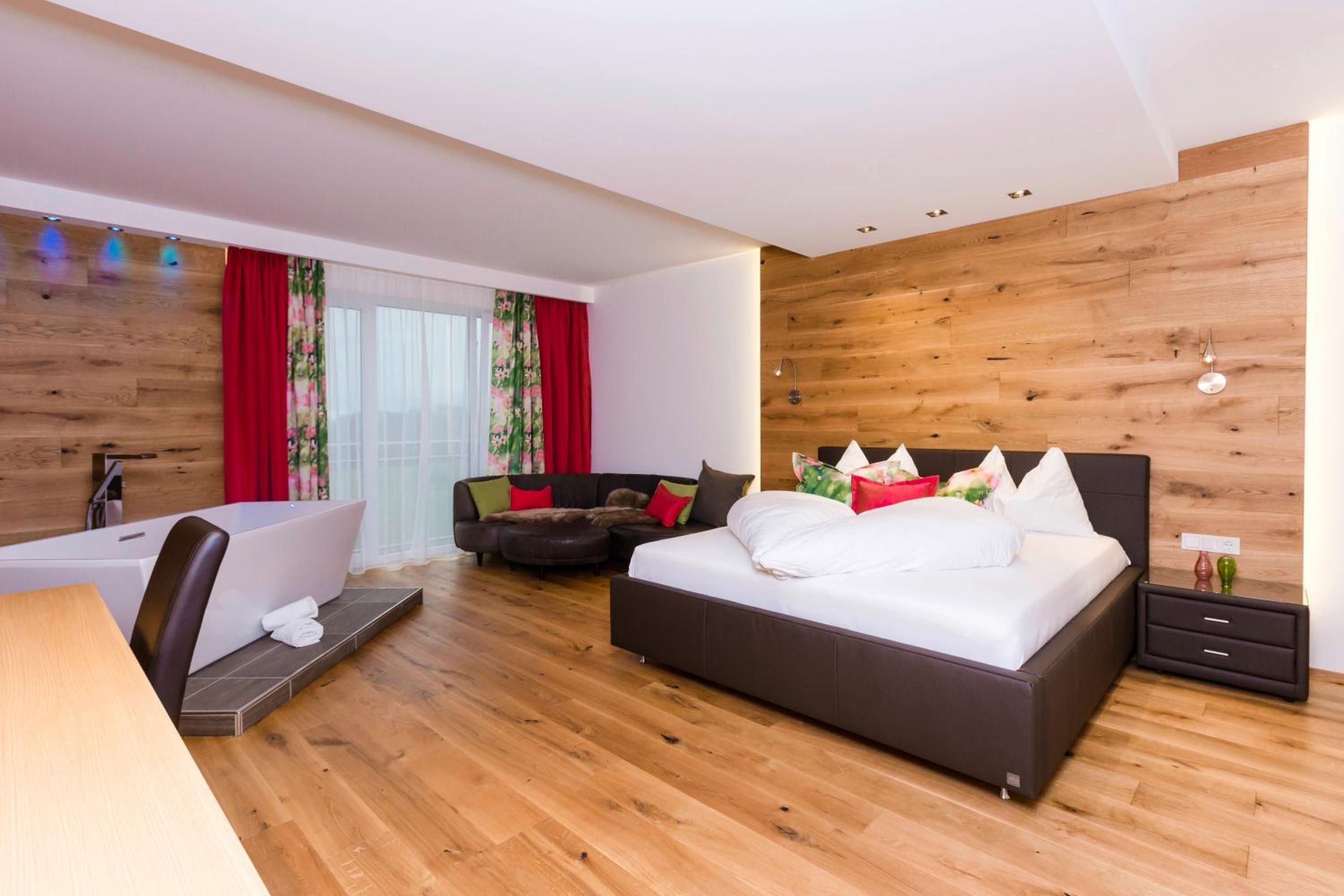 A modern bedroom with a large bed, a sofa, a desk, and a shower area.