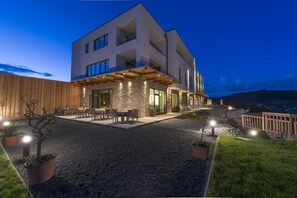 A modern two-story house with a covered patio, outdoor seating, and a view of the surrounding landscape. - Trippelgut Schlafgut (Feldkirchen in Kaernten)
