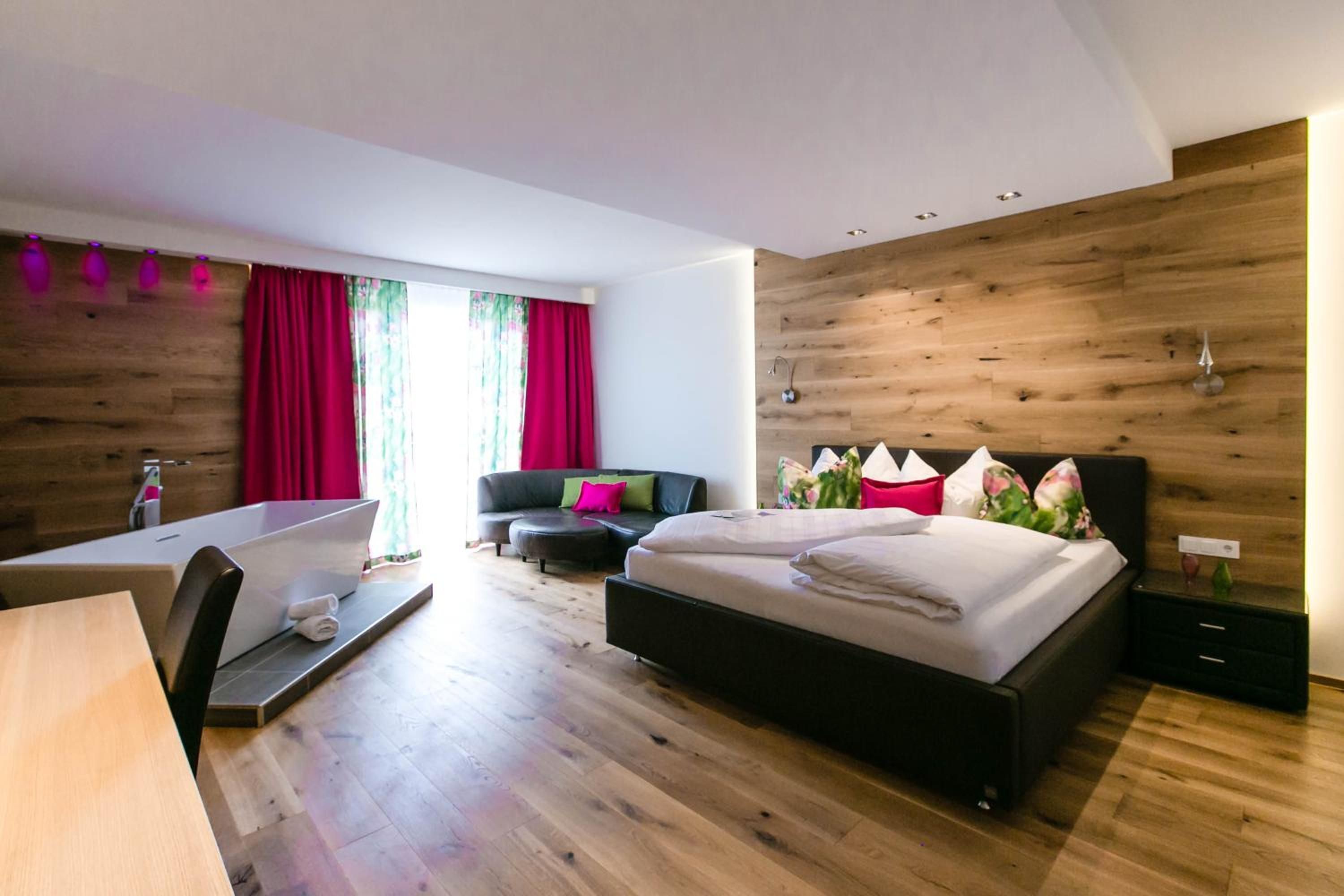 A modern bedroom with a large bed, a sofa, a desk, and a bathroom.