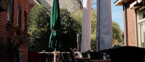 An outdoor seating area with tables and chairs, a green umbrella, and a building with a clock tower in the background.