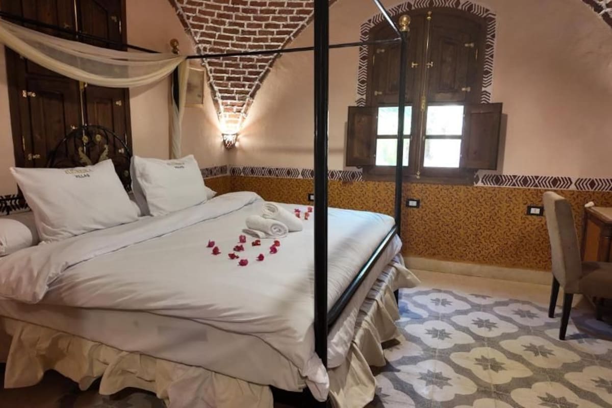 A bed with a canopy, a nightstand, a chair, and a patterned floor.