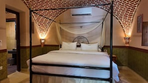 Una cama con dosel y cuatro columnas, un aire acondicionado de pared y dos apliques.