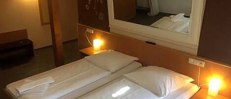 A hotel room with a double bed, bedside lamps, a mirror above the bed, and a wooden headboard.