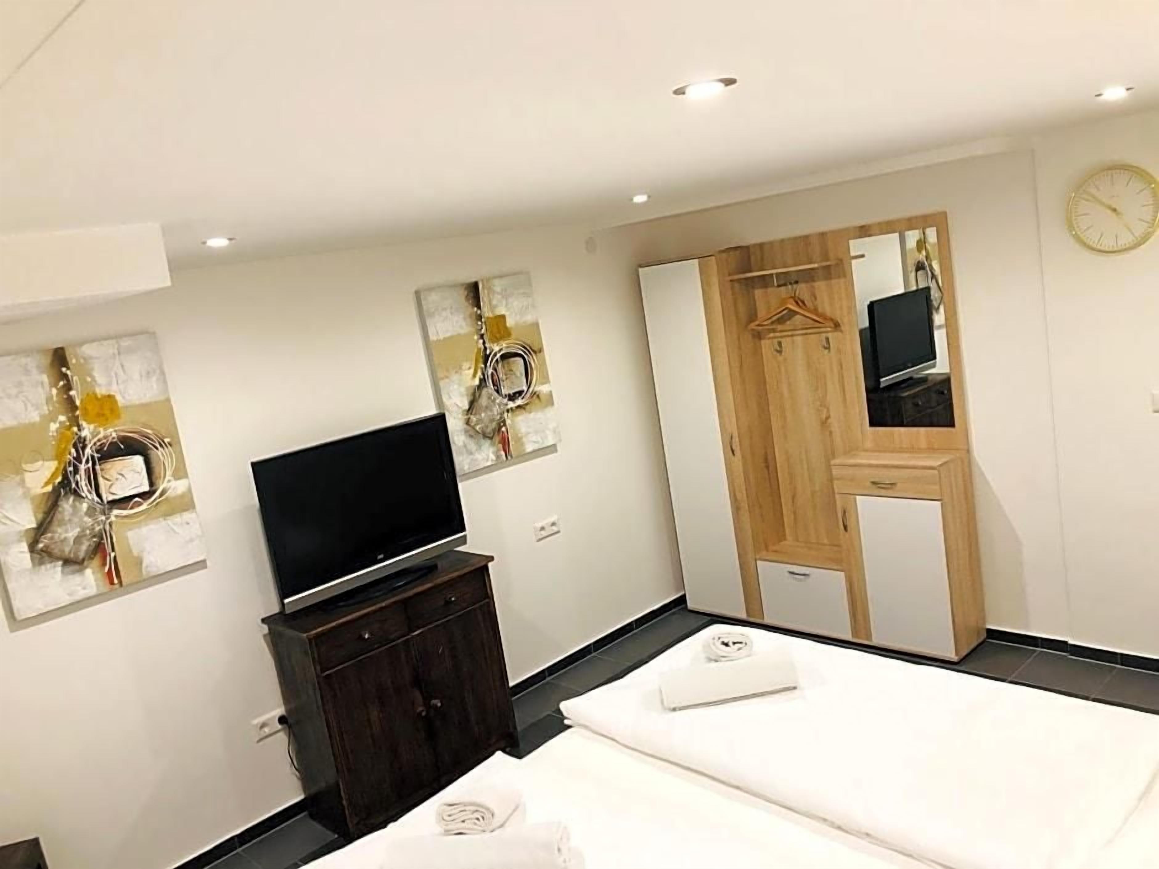 Una habitación de hotel moderna con un televisor de pantalla plana, un armario de madera, un espejo y una cama con una colcha blanca.
