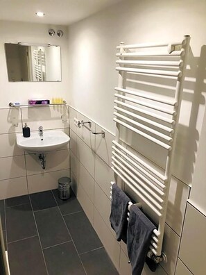 Un baño con un lavamanos blanco, un espejo y un perchero para toallas.
