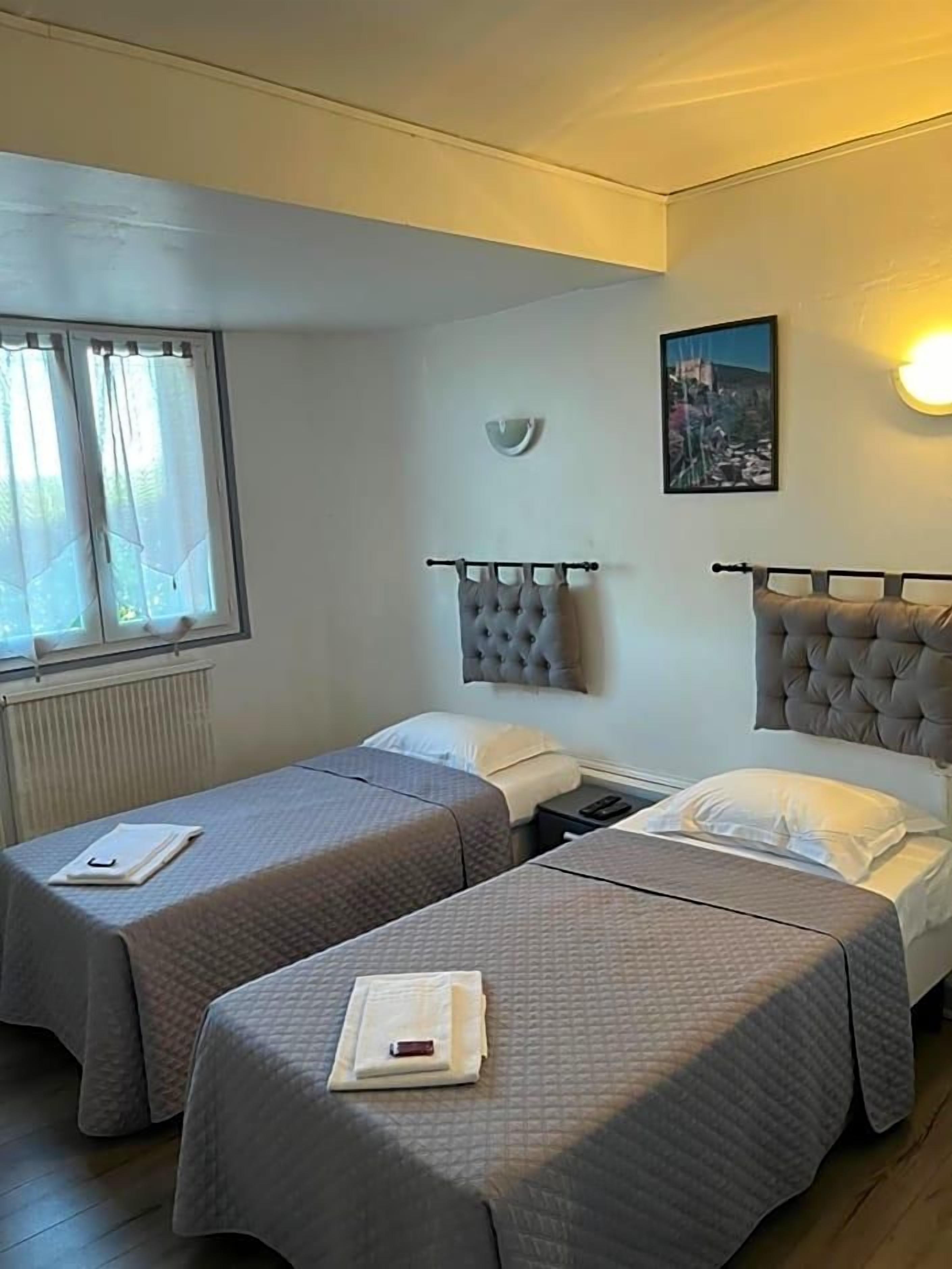 A room with two beds, a window, a wall-mounted light, and a picture.