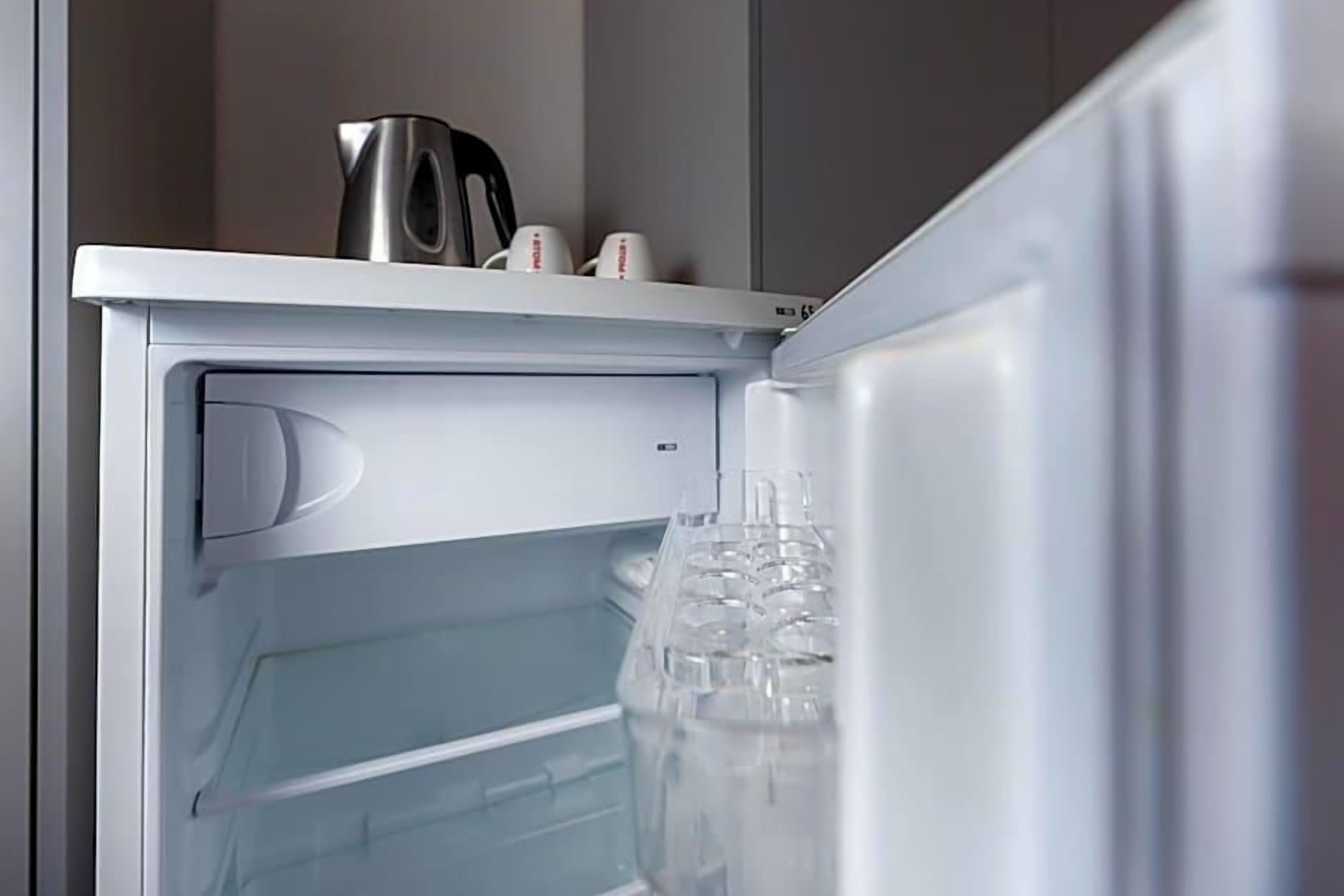 An open refrigerator with a water dispenser and a kettle on top.