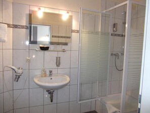 Un baño con un lavamanos blanco, un espejo, cabina de ducha y una puerta de vidrio.
