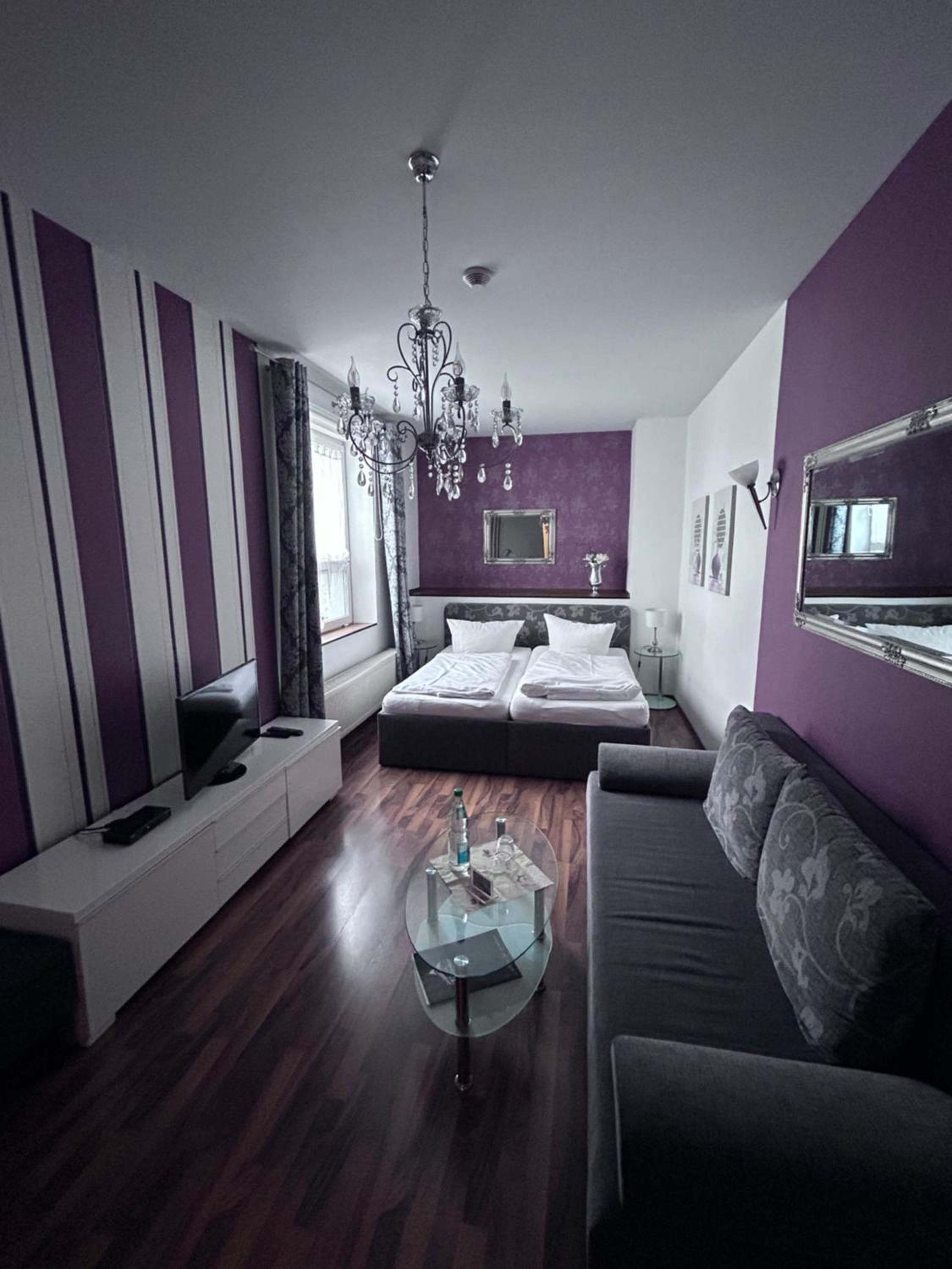 A modern bedroom with a bed, a sofa, a TV, and a chandelier.