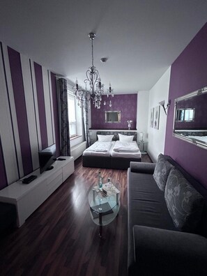 Un dormitorio moderno con cama, sofá, televisión y candelabro.