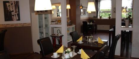 A dining area with tables set for service, chairs, and hanging lamps.