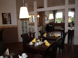 Comedor con mesas dispuestas para el servicio, sillas y lámparas colgantes.