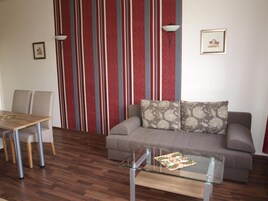 A living room with a sofa, a glass coffee table, a dining table with chairs, and a striped wallpaper.