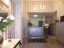 Zona de recepción de un hotel con mostrador, candelabro y recepcionista.