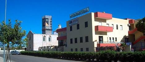 Un hotel llamado 'HOTEL GROTTELE' con una fachada moderna, un estacionamiento visible y un cielo despejado.