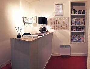 A reception desk with a computer, a lamp, and a wall-mounted display of keys. - Le Mogador (Bayeux)