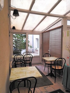 A room with a glass door leading outside, a table with chairs, and a lamp. - Le Mogador (Bayeux)