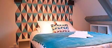 Un dormitorio con pared de estampado geométrico, una cama con manta azul y almohada blanca.