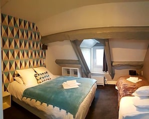 A bedroom with a bed, a bedside table, a window, and a geometric patterned wall. - Le Mogador (Bayeux)
