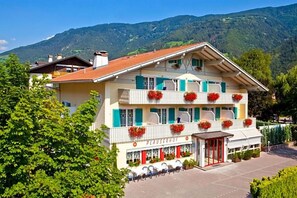A hotel with a traditional Alpine architectural style, featuring a balcony with red flowers, a terrace with outdoor seating, and a mountain backdrop. - Parkhotel Plauserhof (Plaus)