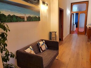A living room with a sofa, a painting on the wall, and a wooden floor. - Hotel Cormorano (Pedaso)