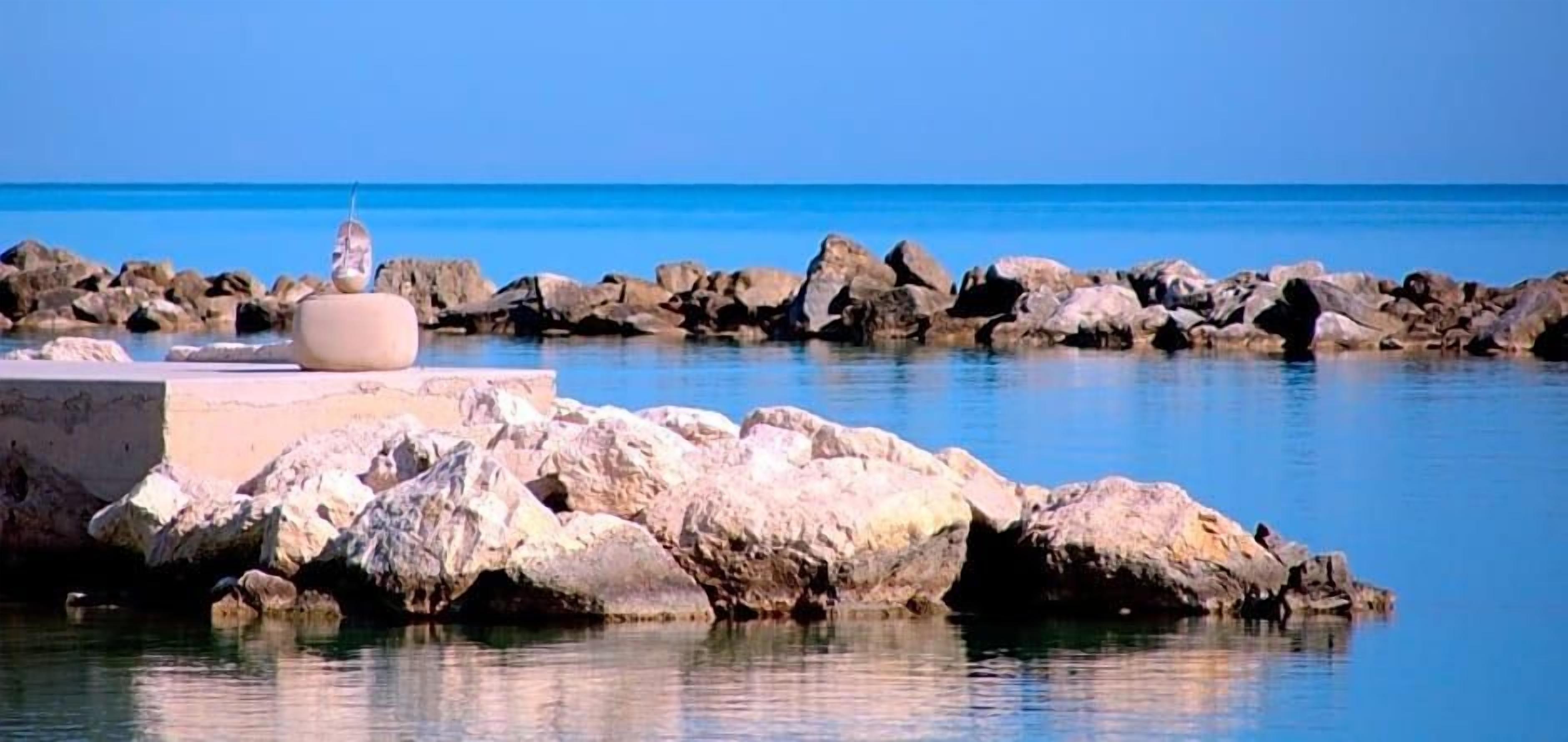 Una riba rocosa amb aigua tranquil·la i un cel serè.
