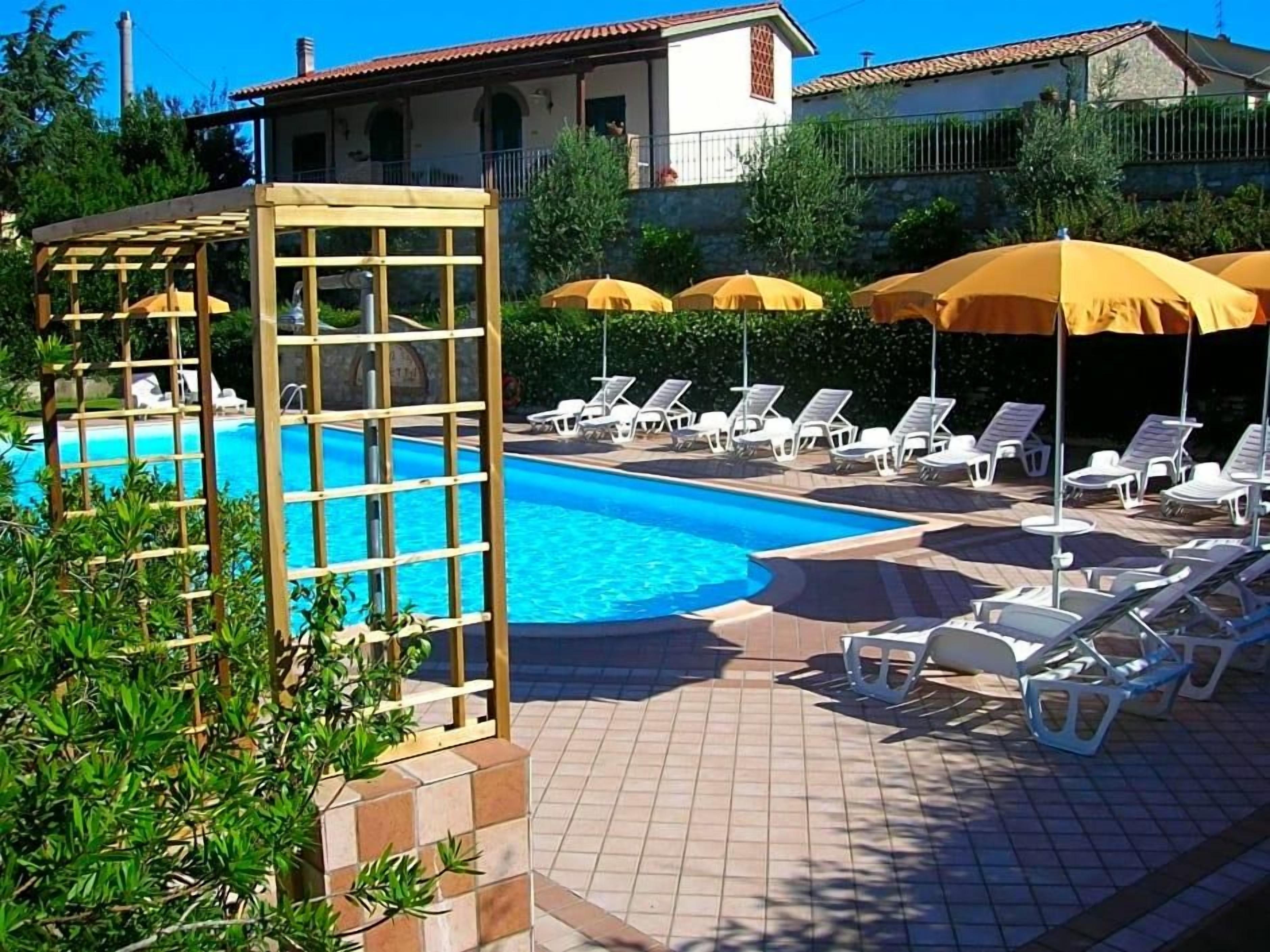 Una piscina con tumbonas y sombrillas, rodeada de un patio empedrado.