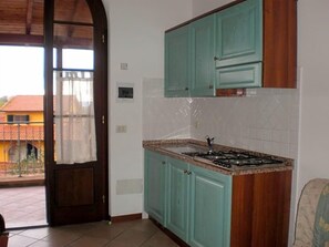 A kitchen with teal cabinets, a gas stove, and a view through an open door to an outdoor area.