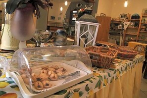 A buffet table with a variety of food items, including a covered dish with pastries and a wicker basket with bread.