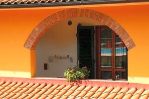 A building with an orange facade, a tiled roof, and a brick archway leading to a door with shutters. - Locanda La Gozzetta (Santa Luce)