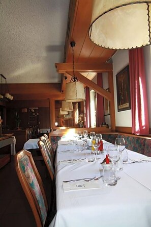 Un interno ristorante con travi in legno, tovaglie bianche e tende rosse.