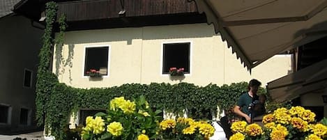 A building with a sloped roof, two windows with flower boxes, and a stone wall in front.