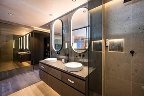 A modern bathroom with two round mirrors, a large vanity with a sink, and a glass-enclosed shower area. - Alpine Spa Resort Viktoria (Avelengo)