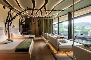 A modern bedroom with a wooden floor, multiple beds, a hanging chair, and a view of the outdoors. - Alpine Spa Resort Viktoria (Avelengo)