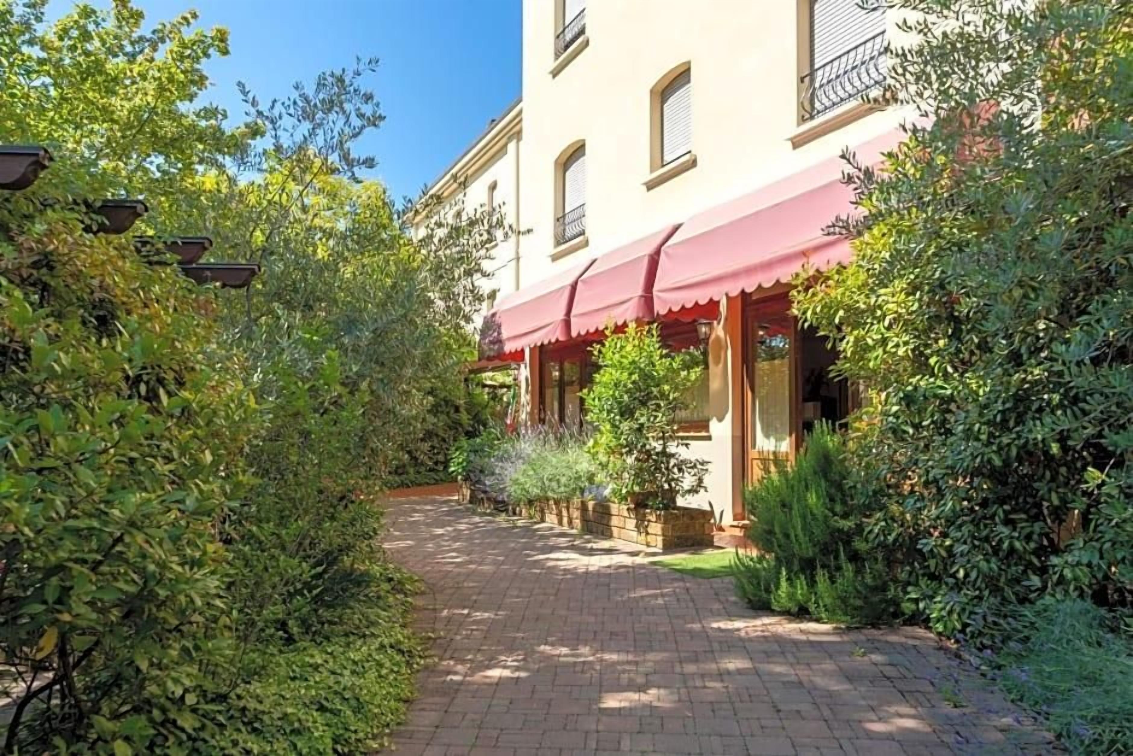 A pathway leading to a building with a red awning, surrounded by lush greenery.
