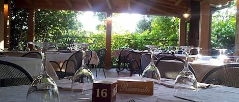Un espacio exterior para comer con mesas preparadas para dos, bloques numerados y copas de vino.