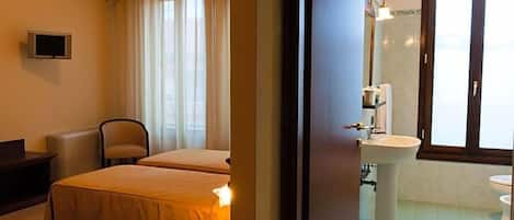 A hotel room with two beds, a television, a chair, a bedside table, a sink, and a window with curtains.