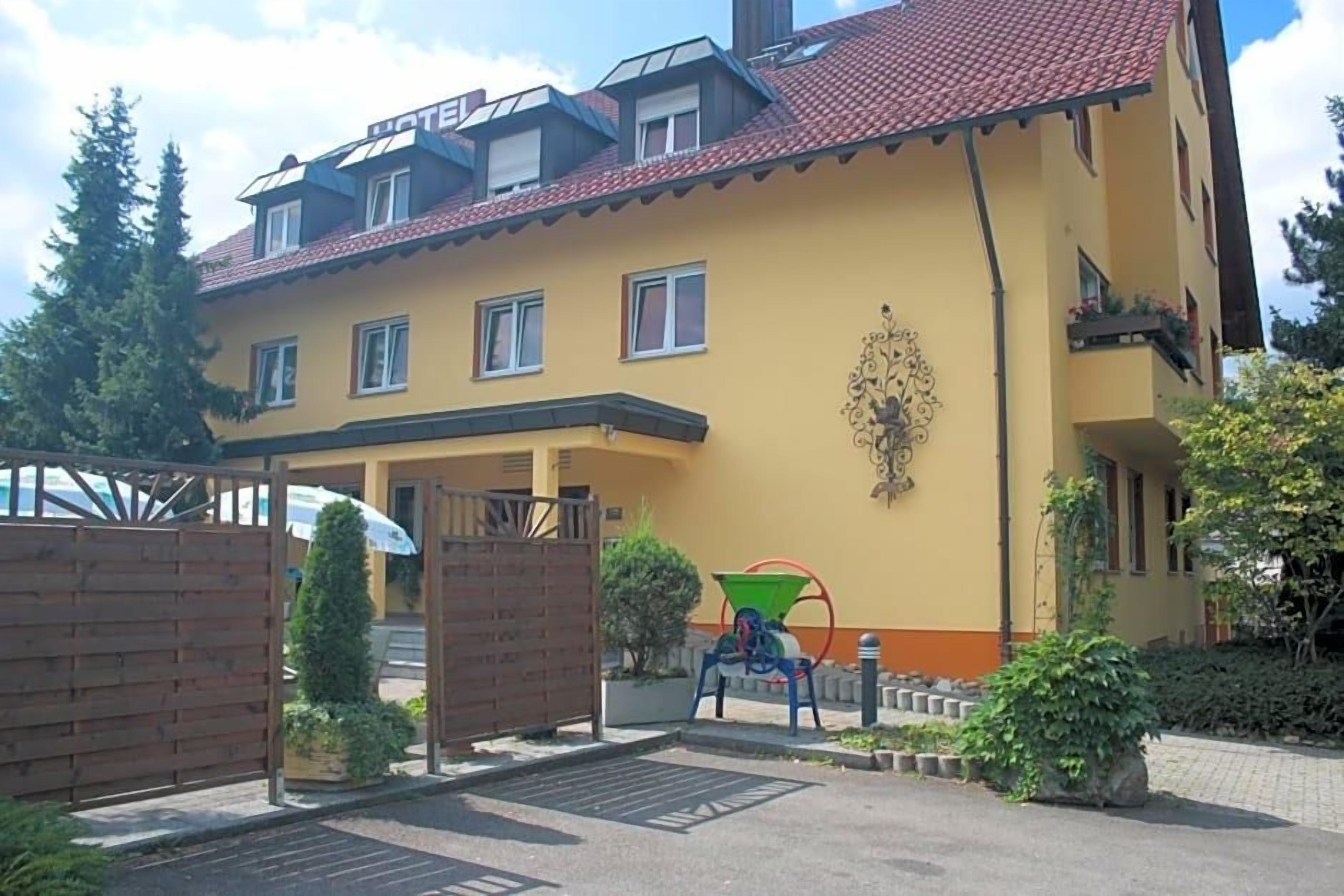 Ein zweigeschossiges Gebäude mit einer gelben Fassade und einem roten Ziegeldach, mit einem befestigten Eingangsbereich und einem kleinen Garten.